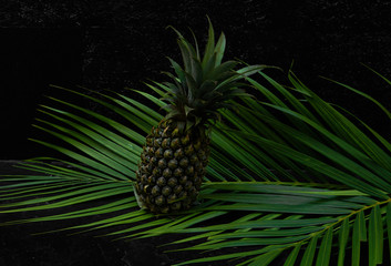 green tropical palm leaves and pineapple mockup on natural black stone background with copyspace top view.