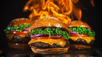 Tasty cheeseburgers, lying on vintage wooden cutting board, fire flames in background.
