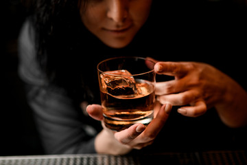 close-up of glass with alcoholic drink and ice in woman hands