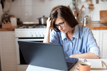 Upset woman working from home office. Worry freelancer using laptop and the Internet. Workplace in...