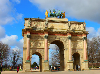 Fototapeta na wymiar A large stone gate monument with a chariot and horses on top. Entrance to the Tuileries Park in Paris with tourists walking near the arch.
