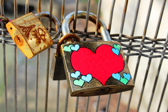 Hanging on the bridge a few padlocks of iron. One lock with a red big heart and a few light green color small hearts.