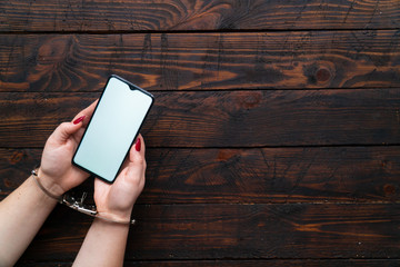 Woman hands in handcuffs hold a smartphone on a wooden background. The concept of internet and gadget dependency.