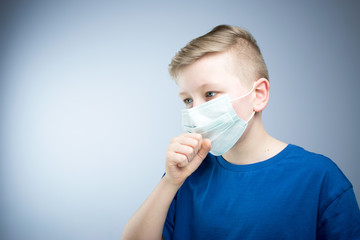 The boy coughs in his hand. A child in an antiviral mask.
