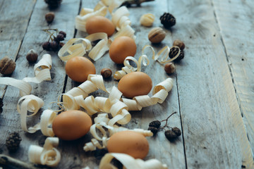 Raw natural gold eggs with nature details, nuts, cones and wood shavings on an old vintage wooden...