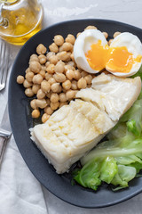 fried cod fish with chick pea, boiled egg and cabbage on dark dish