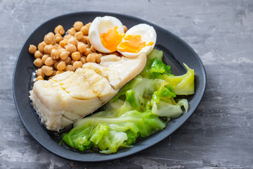 fried cod fish with chick pea, boiled egg and cabbage on dark dish