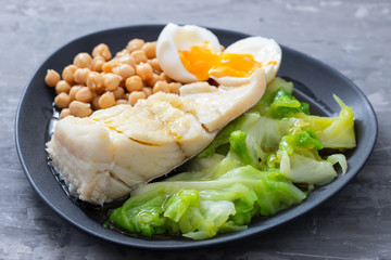 boiled cod fish with cabbage, chick pea and egg on dark dish