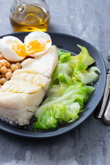 boiled cod fish with cabbage, chick pea and egg on dark dish
