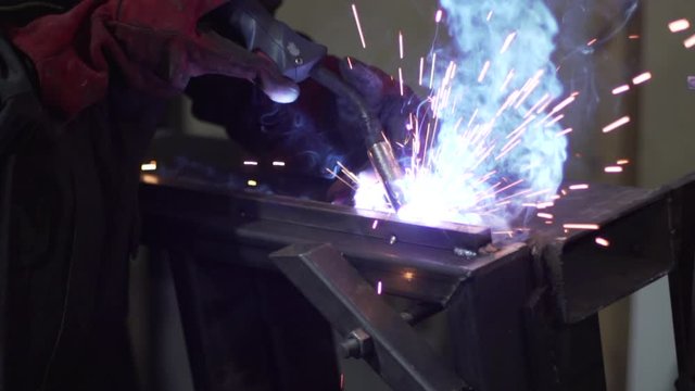 A welder welds metal parts using a welding machine. Detailed close-up.