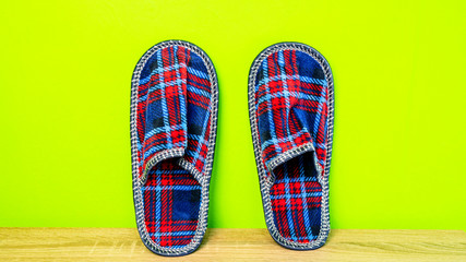 A pair of colorful comfortable, cushioned, checkered disposable slippers leaned against yellow wall. Close-up.