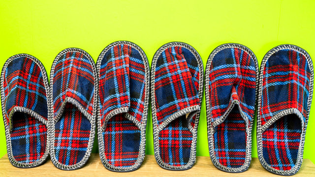 A lot of  of colorful comfortable, cushioned, checkered disposable slippers leaned against yellow wall. Close-up.