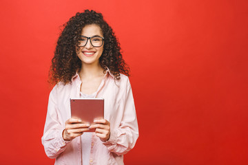 Beautiful curly young girl smiling using tablet isolated over red background. Copy space.