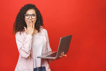 Portrait of happy shocked surprised woman standing with laptop computer isolated on red background.