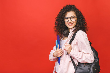 Young curly student woman wearing backpack glasses holding books and tablet over isolated red background. - 329900321