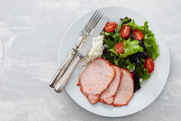 fried pork with boiled rice and salad on white plate on ceramic background
