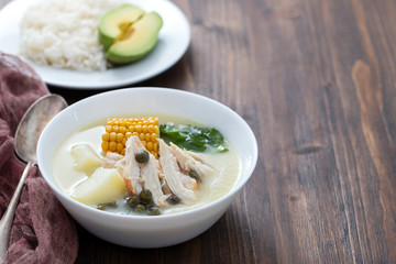 soup potato with corn and chicken in white bowl and plate with boiled rice and avocado on ceramic background