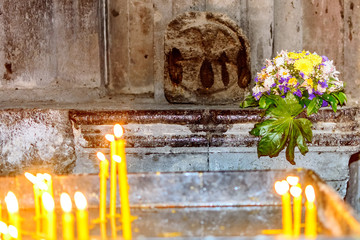 Two groups of candles in a medieval Armenian apostolic church in the foreground in defocus and a bouquet of flowers in the background, focus on flowers