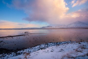 Dark clouds developing in a blue sky with a pink horizon over the coast of Iceland at sunset, with a rocky shoreline in the foreground  