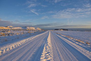 Looking down a straight road in a snow covered landscape in southern Iceland , late afternoon in...