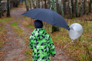 The sad boy was cold and wet from the rain. The boy with the balloon took shelter from the rain under a black umbrella.
