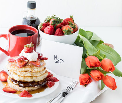 Close up view of a tray table filled with breakfast items, tulips and a card for Mother's Day.