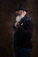 Studio portrait of handsome mature bearded man in the black top hat against the dark wall, selective focus
