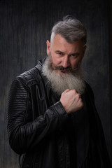 Studio portrait of handsome mature gray-haired bearded man in a leather jacket, selective focus