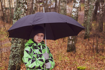 A teenage boy walks alone with an umbrella in the forest, Park. It's raining. Loneliness and autumn.