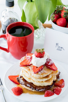 A close up of a stack of pancakes with strawberries and maple syrup for Mother's Day.