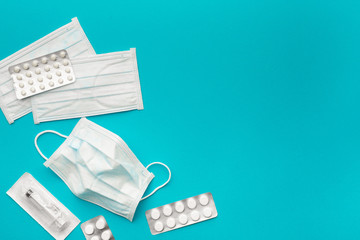 Medical protective masks, disposable syringe in sterile packaging and pharmaceutical packaging with pills on paper, blue bright background. The concept of protecting health from the virus. Copy space