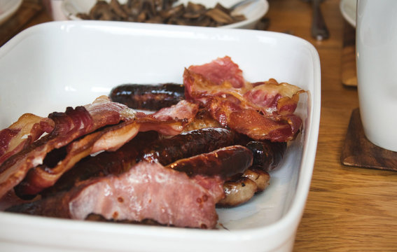 Greasy fried bacon and sausages on a white ceramic plate - typical English breakfast