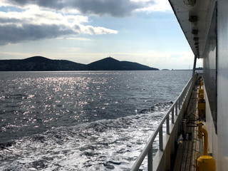 A ship in motion sailing on waves on a partly cloudy day with an island on larboard