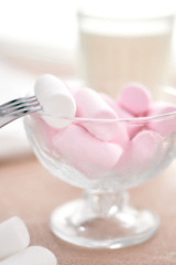 marshmallows in a glass bowl stands on a light table with a fork and milk.