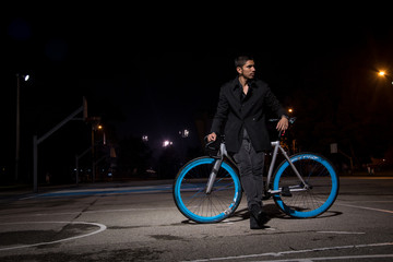 young man in black lying on his bike in a dark park at night.  