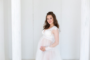 a pregnant girl in a white negligee hugs her stomach with her hands