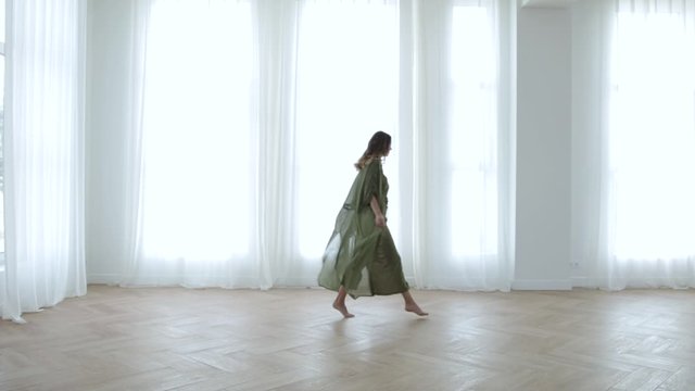 a girl in a long dress walks around the apartment smiling, white curtains
