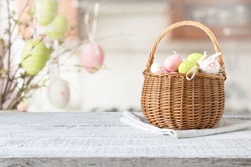 Wicker basket with easter colorful eggs on kitchen wooden table. Spring easter composition. Space...