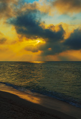 The sun rises over the sea and shines through the clouds