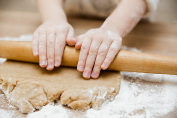 Baby girl is preparing in kitchen.Little hands with rolling pin,dought and flour on the wooden table.Close up view