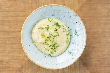 Mashed potatoes with dill in plate on a wooden background