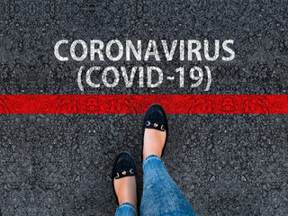 A woman steps to red line and words Coronavirus COVID-19 on asphalt road