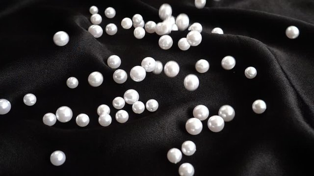 White pearls fall on black fabric. Slow motion.