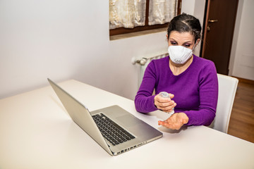 Coronavirus, Covid-19. Stay at home. Quarantine. Protection mask. A Caucasian woman forced to stay home to prevent virus infection, works on the laptop. Smart Working. Disinfect hands with gel.