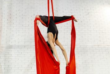 brunette girl dressed in black color performing aerial dance with red fabrics on white wall