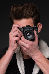 A beautiful young brunette in a dark jacket with a camera in his hands on a dark background
