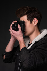A beautiful young brunette in a dark jacket with a camera in his hands on a dark background - 329915315