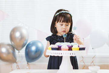 toddler girl decorating cupcake for her birthday party against window background