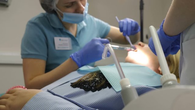 Dental clinic concept. Dentist examining young famale patient. close-up. Cooperation of doctor and assistant. Stomatologist holding dental tools. In Modern Dental Office. 4 k video