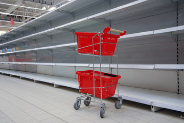 shopping trolley with empty baskets against empty shelves in grocery store